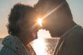 portrait and close up of two happy in love seniors looking to each other smiling with the sun of the sunset between their heads